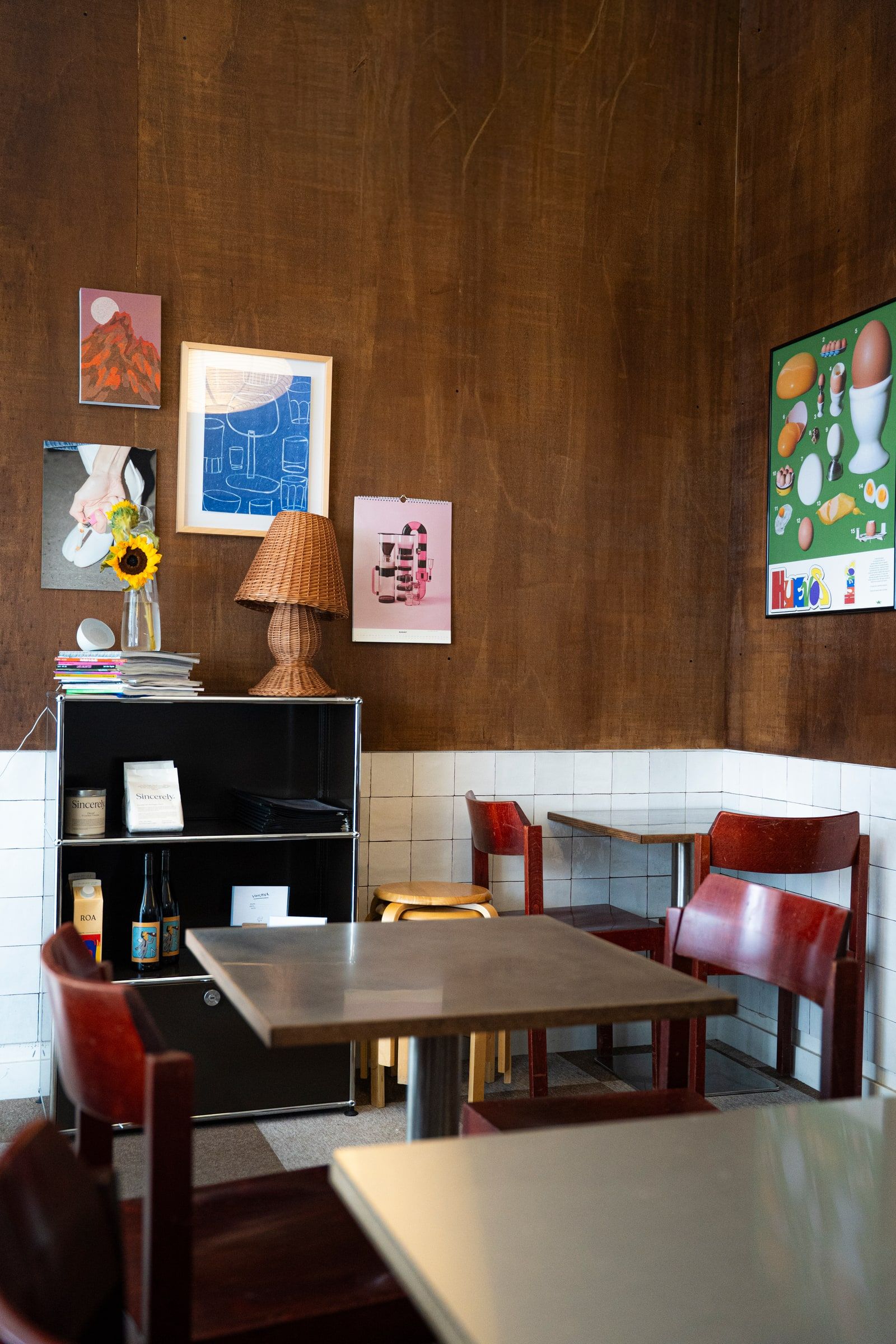 A corner of the cafe with wood-panelled walls, red chairs and a sunflower on the shelf