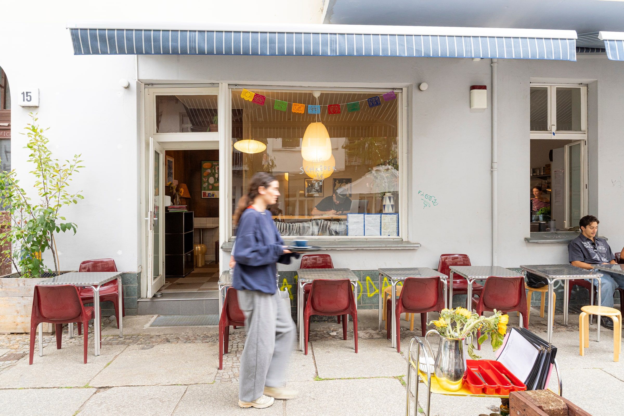 The front of the cafe, with red chairs on the pavement under a striped awning