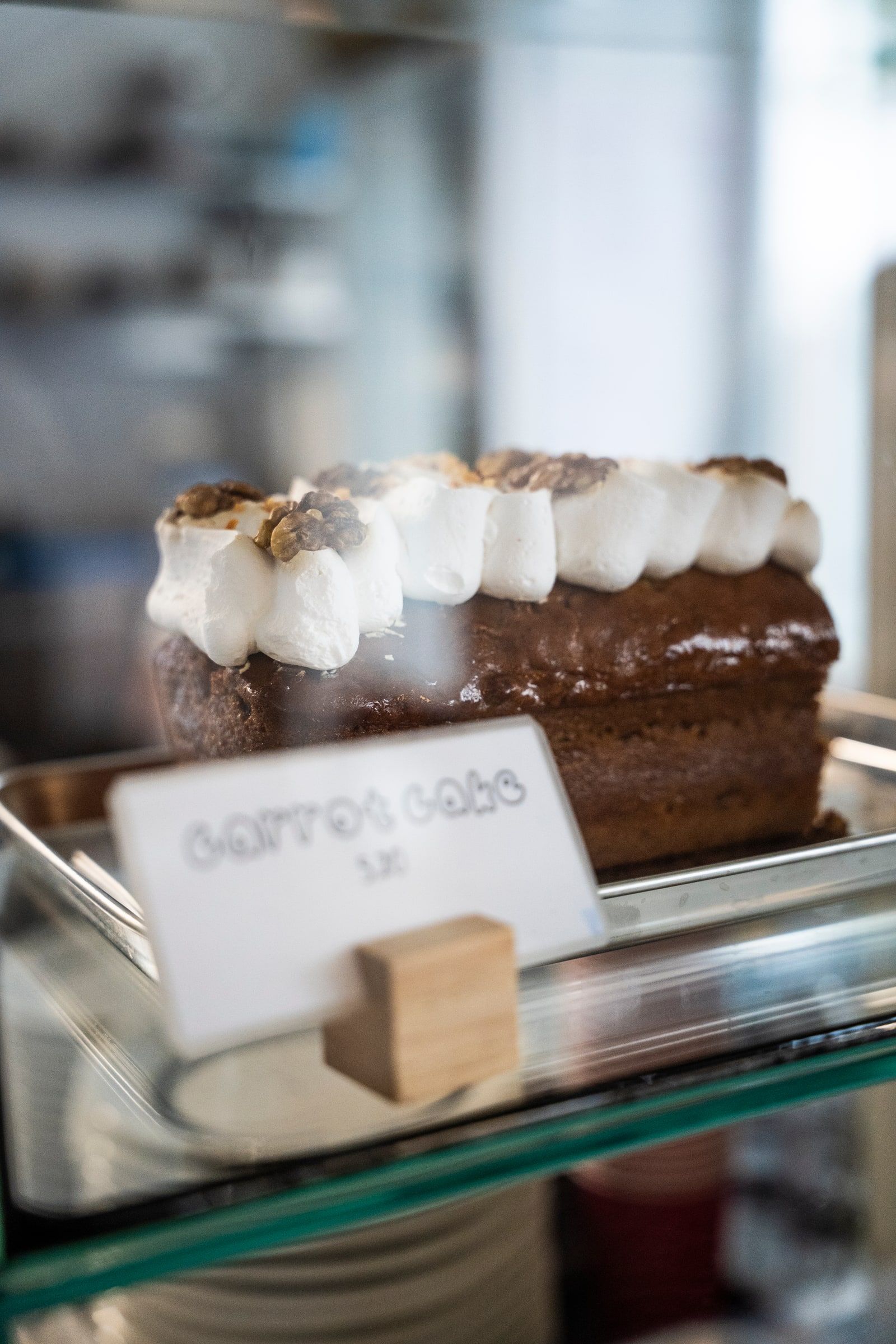 A carrot cake topped with piped white icing and walnuts, in the counter display